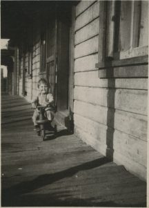 Three year old Mel Fletcher riding a tricycle on the porch of the Fletcher home on Park Avenue in Park City, 1921-22.